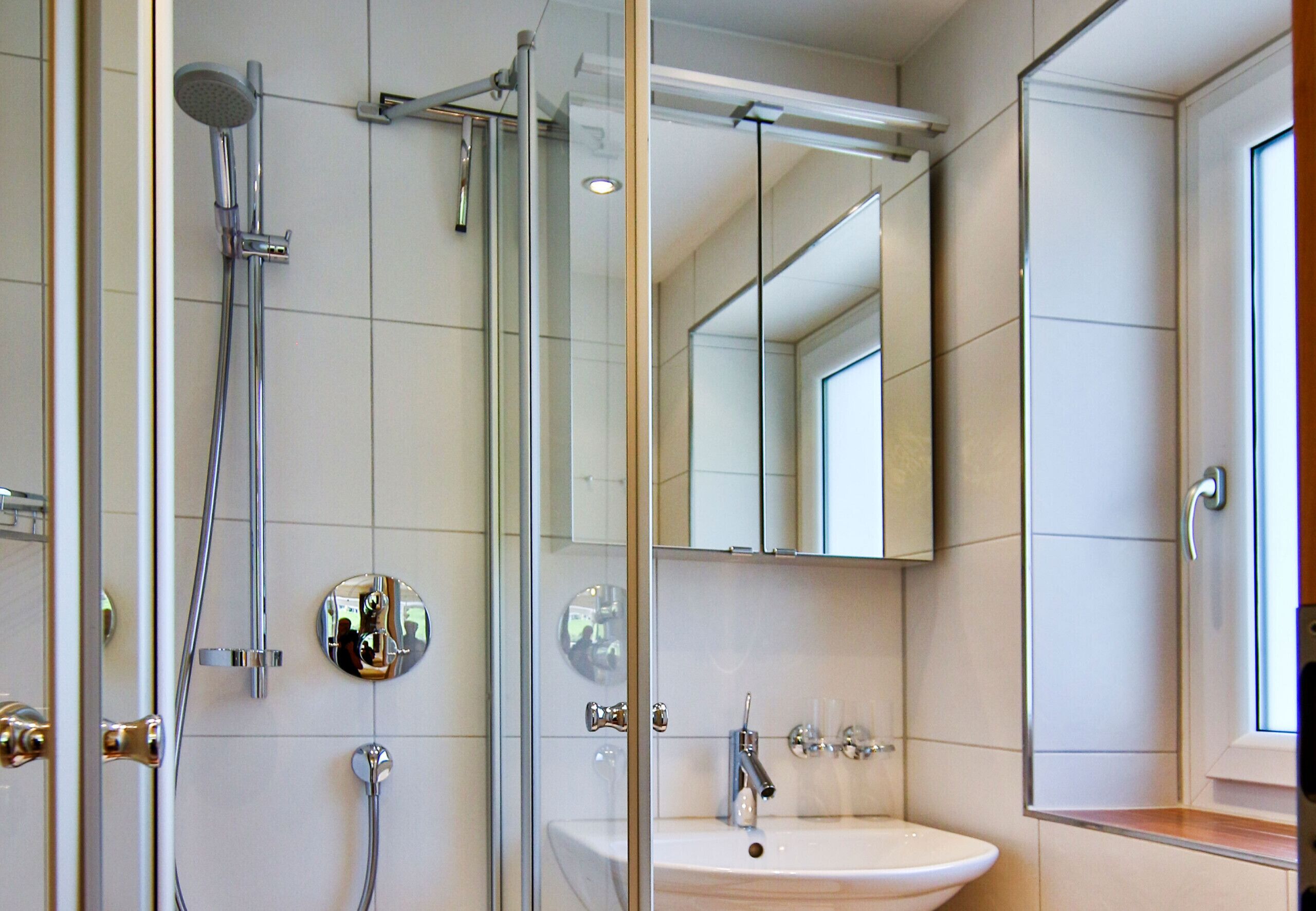 Un baño moderno con ducha de vidrio, lavamanos con espejo y ventana que proporciona luz natural.