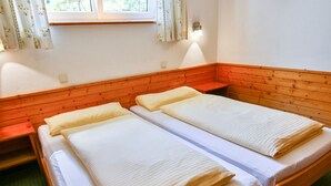 Une chambre avec deux lits simples, des têtes de lit en bois, une petite table et une fenêtre avec des rideaux.