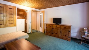 Une pièce avec un plafond en bois, un téléviseur posé sur un meuble en bois, un banc et un tapis à motifs.