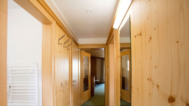 Un couloir en bois, avec un tapis vert, des portes en bois et un plafond blanc.