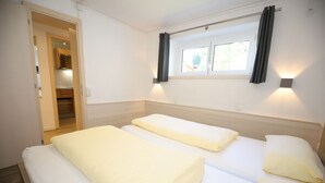 Hotellihuone, jossa on kaksi sänkyä, ikkuna, jossa on verhot, ja näkyvissä oleva keittiöalue.