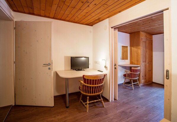 Una habitación con techo de madera, un escritorio con televisor, dos mecedoras y una puerta.