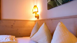 A bed with white bedding and pillows, a wooden headboard, and a wall-mounted light fixture.