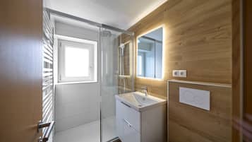 Une salle de bain moderne avec une douche à parois de verre, un lavabo blanc et un panneau mural en bois.