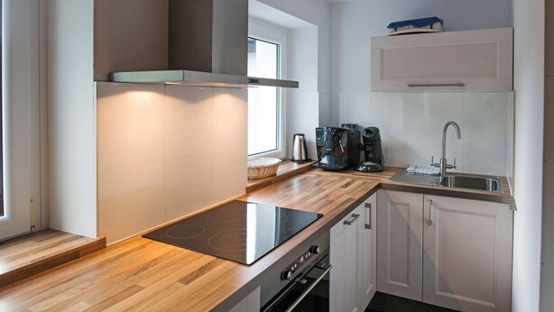 Une cuisine moderne dotée d’un plan de travail en bois, d’un four encastré et de meubles blancs.