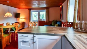 Une cuisine chaleureuse avec des meubles de rangement en bois, une table à manger avec des chaises et une grande fenêtre agrémentée de rideaux.