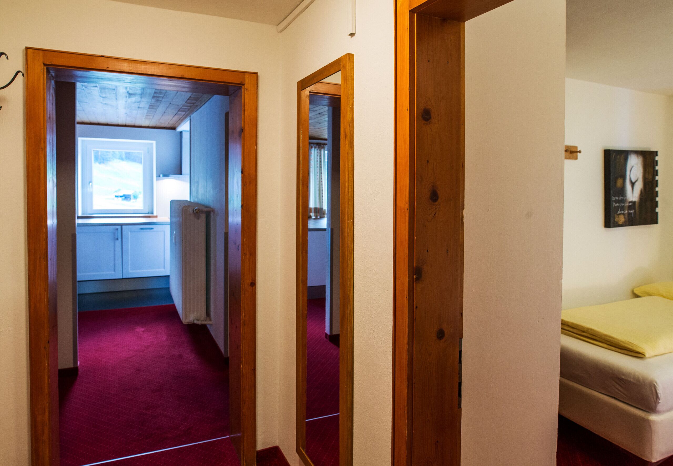 Un corridoio stretto con porte in legno che conducono a una stanza con un letto e un quadro appeso al muro.