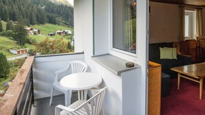 Un balcon avec une table et des chaises, une fenêtre donnant sur un paysage verdoyant et un intérieur en bois avec un canapé et une table.