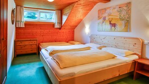 A bedroom with two beds, a wooden dresser, a window with curtains, and a painting on the wall.