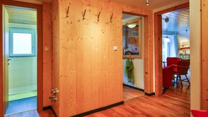 A wooden door with a handle, a hallway with wooden flooring, and a red chair in the background.