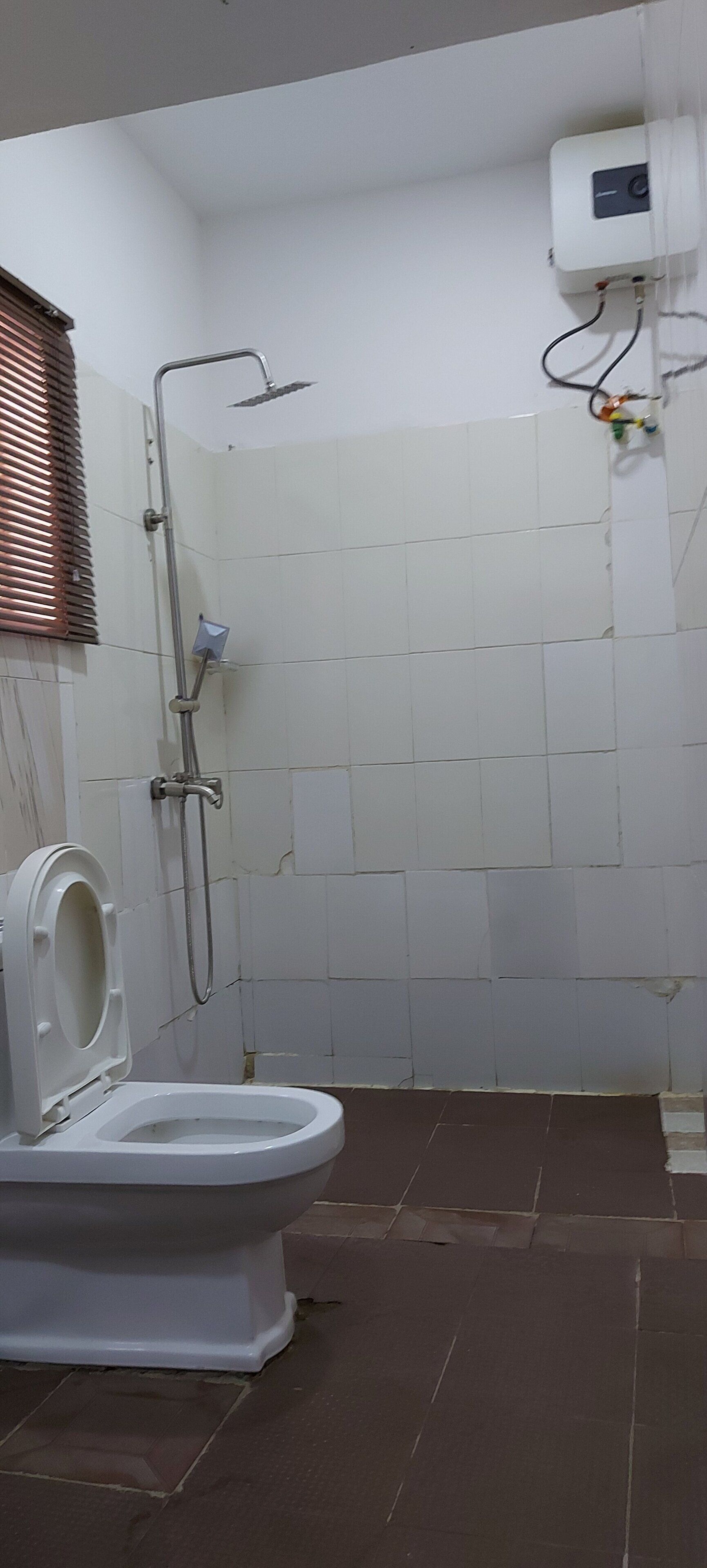 A bathroom with a toilet, shower, and a wall-mounted air conditioning unit.