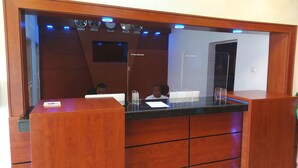 A reception desk with a wooden finish, a digital clock displaying time in multiple cities, and a sign for the Peace Media Hotel. - Peace Media Hotels Gwarimpa (Abuja)
