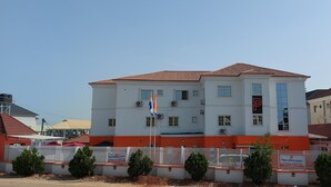 A multi-story hotel with a red-tiled roof, white walls, and a fenced perimeter. - Peace Media Hotels Gwarimpa (Abuja)