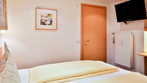 Ein Hotelzimmer mit einem Bett, einer Holztür, einem gerahmten Bild an der Wand und einem Fernseher über einem Heizkörper.