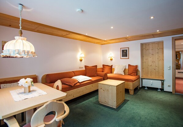 Ein gemütliches Wohnzimmer mit Holzboden, einem Esstisch mit Stühlen, einer Couch und einem Holzschrank.