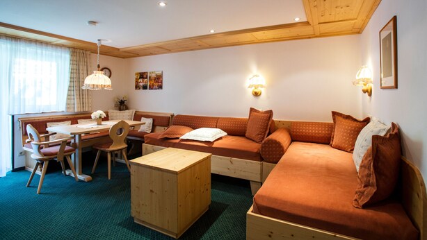 Ein gemütliches Zimmer mit Holzbalkendecke, einer Couch, einem Esstisch mit Stühlen und einem kleinen Holztisch.