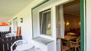 Ein Zimmer mit einem kleinen Tisch, Stühlen, einem Vorhangfenster und einer Holztür zu einem weiteren Raum.