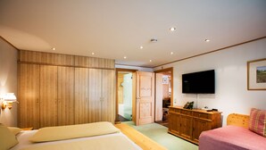 Une chambre à coucher avec un grand lit, un plus petit lit, une télévision, des meubles en bois et une porte donnant sur une autre pièce.
