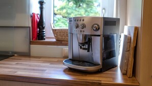 Une machine à café est posée sur un plan de travail en bois, près d’une fenêtre donnant sur un paysage verdoyant.