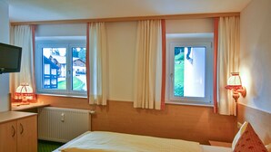 Una habitación de hotel con dos camas, televisión, lámpara y ventana con cortinas.