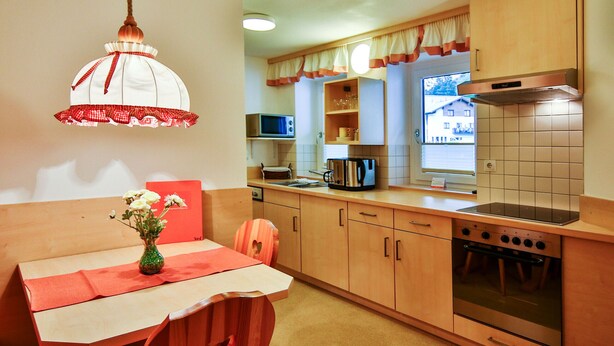 Cocina compacta con armarios de madera, microondas, estufa y comedor con mesa y sillas.