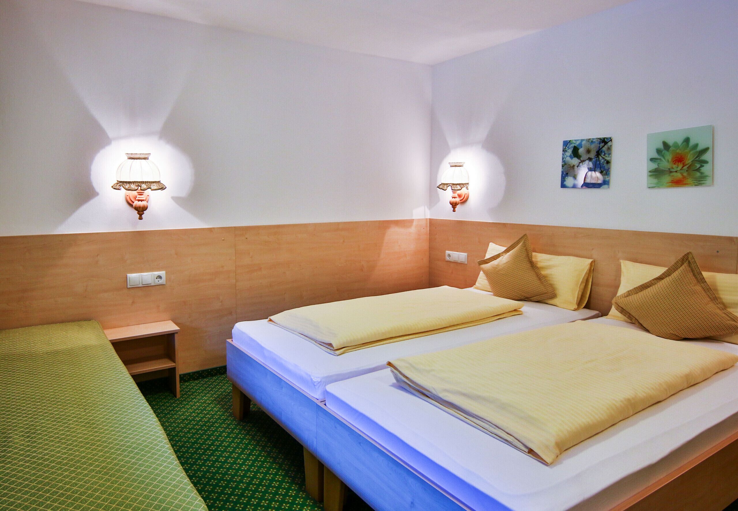 Ein Hotelzimmer mit zwei Einzelbetten, einem Holz-Kopfteil, zwei Wandlampen, einem kleinen Regal und zwei Wandbildern.