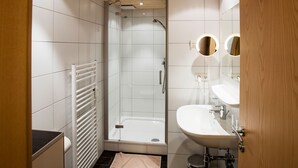 A modern bathroom with a glass-enclosed shower, a white sink, and two round mirrors.