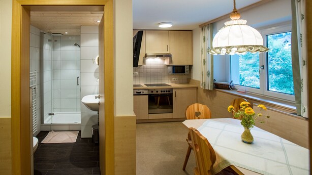 A compact kitchen with a microwave, oven, and sink. There's a dining table with a vase of flowers and a window with a view.