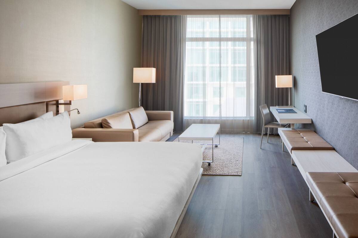 A hotel room with a large bed, a sofa, a desk, and a TV.