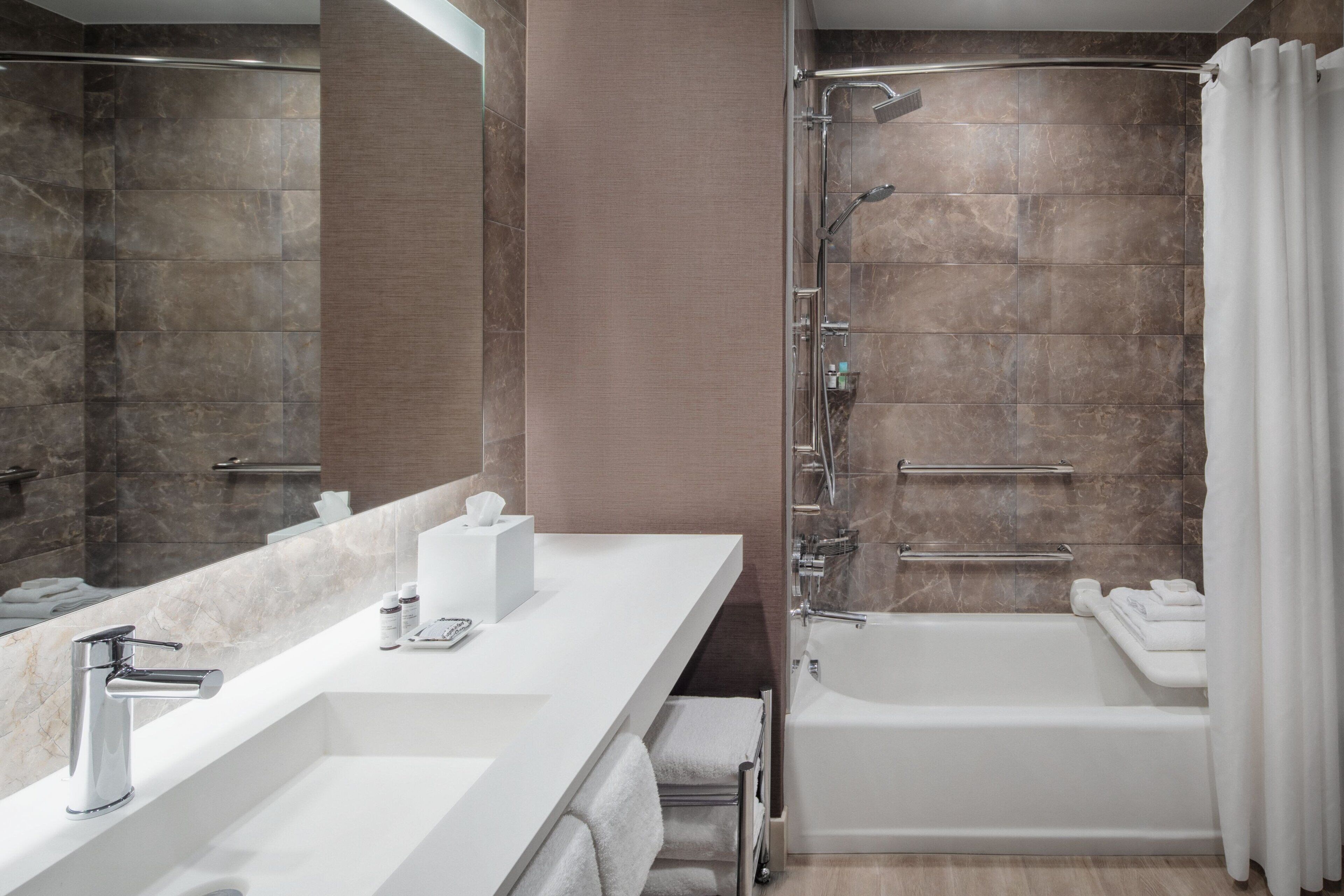 A modern bathroom with a large mirror, a white sink, a bathtub, and a shower area.