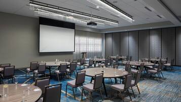 A conference room with multiple tables and chairs, a large screen, and a carpeted floor.