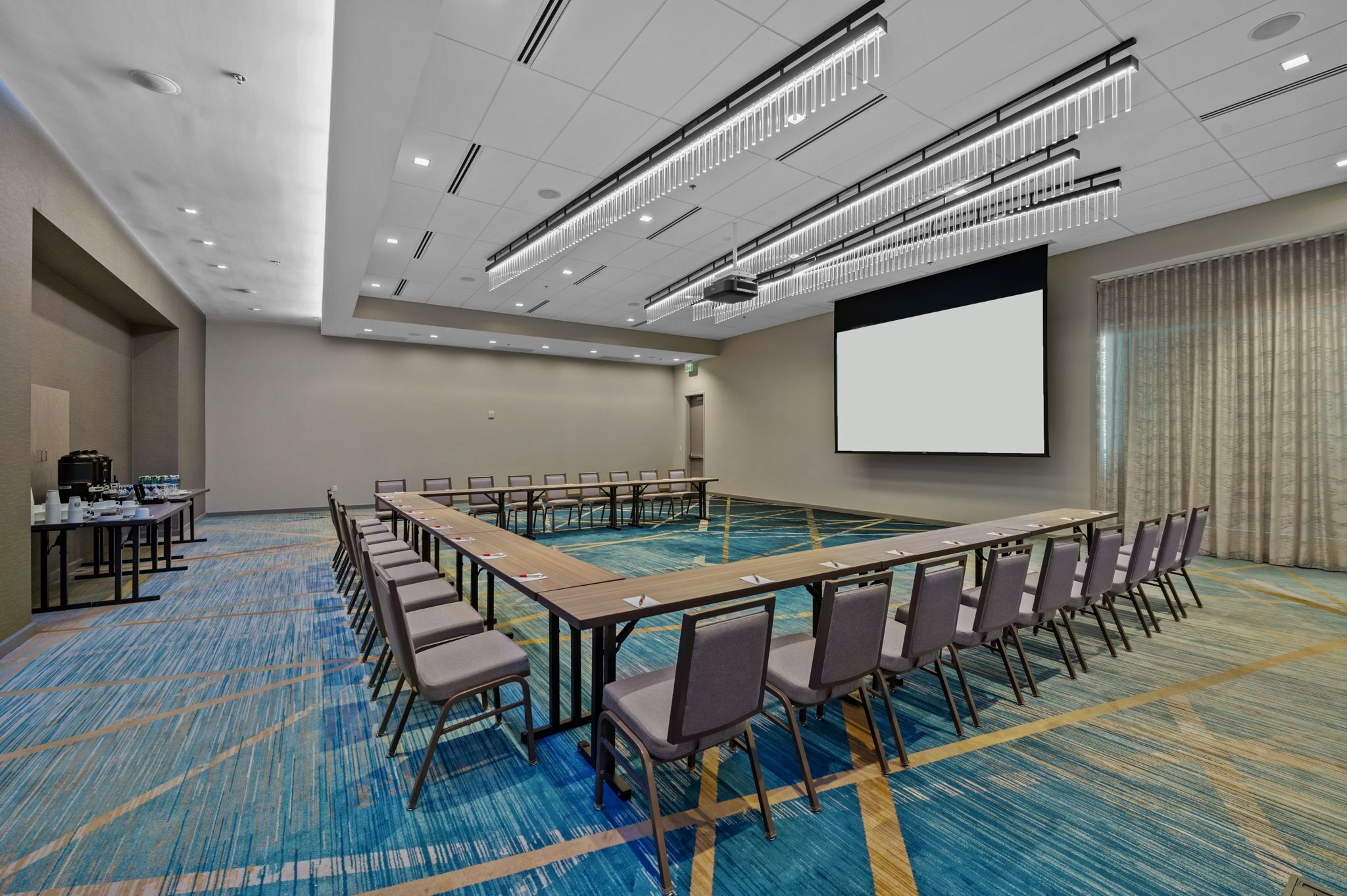 A conference room with a long table, chairs, a projector screen, and a carpeted floor.