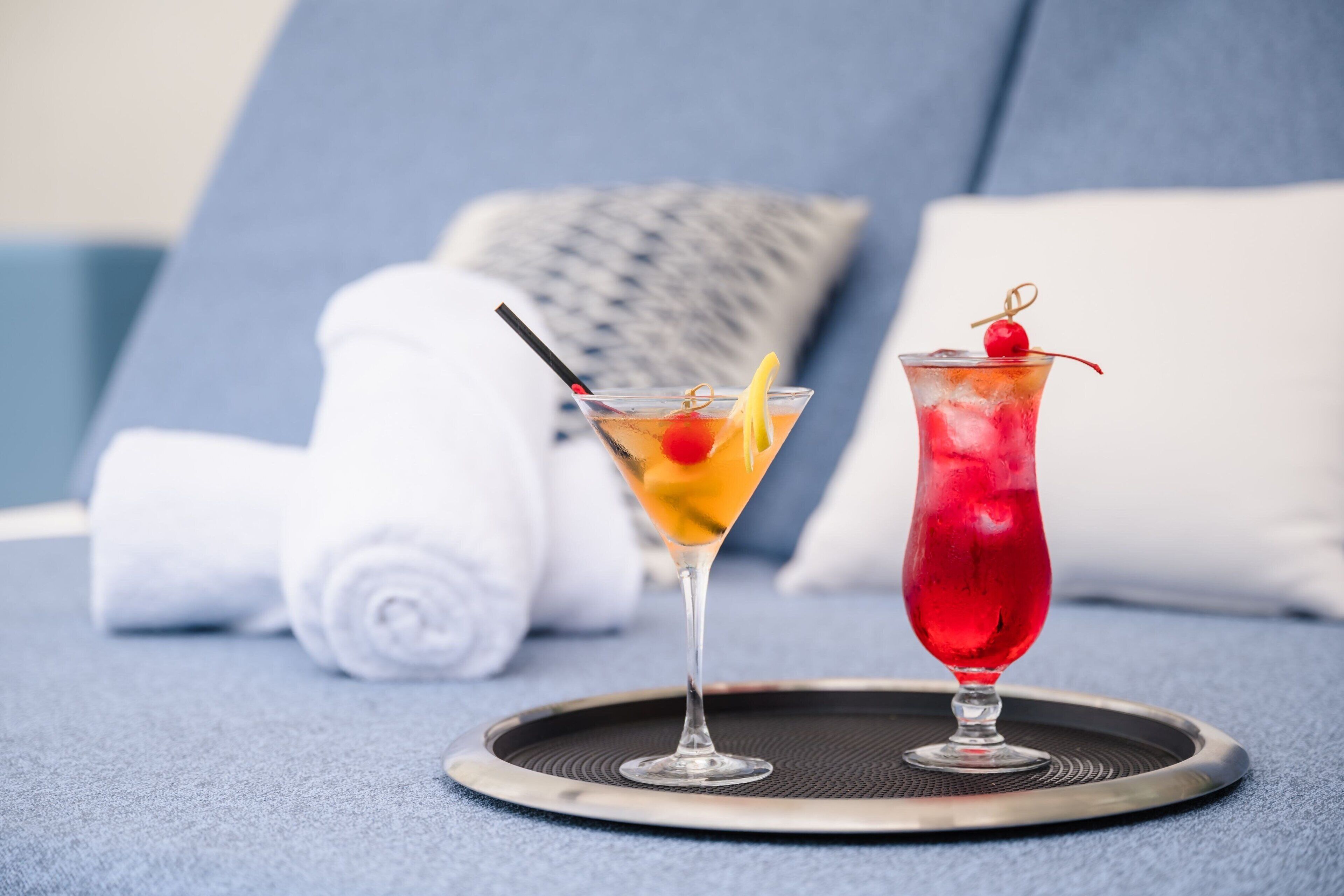 Deux cocktails sur un plateau, avec un canapé bleu et une serviette blanche roulée en arrière-plan.