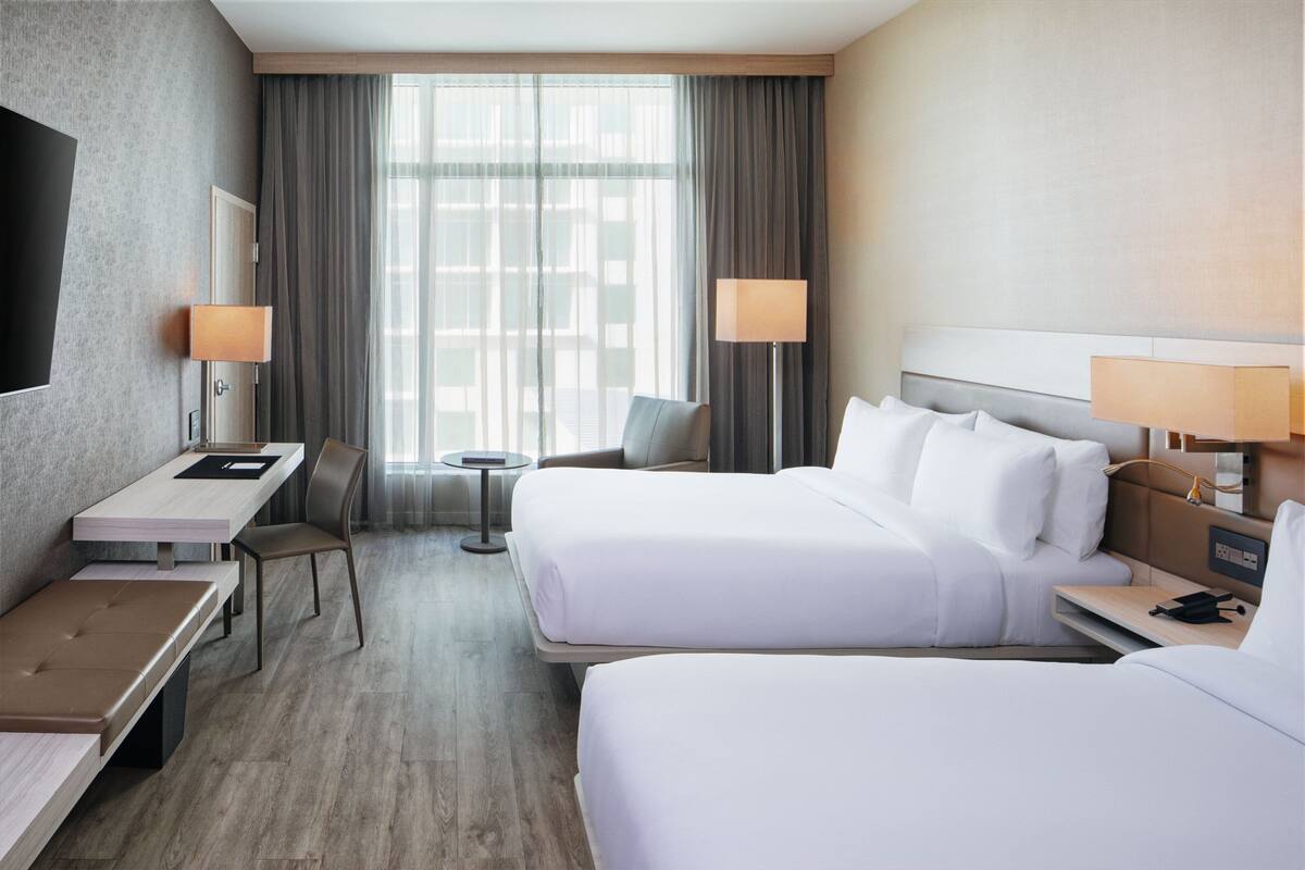 A hotel room with two beds, a desk, a chair, a TV, and a window with curtains.