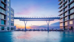 A modern pool area with a pergola, surrounded by high-rise buildings, during sunset. - AC Hotel by Marriott Fort Lauderdale Airport (Dania Beach)