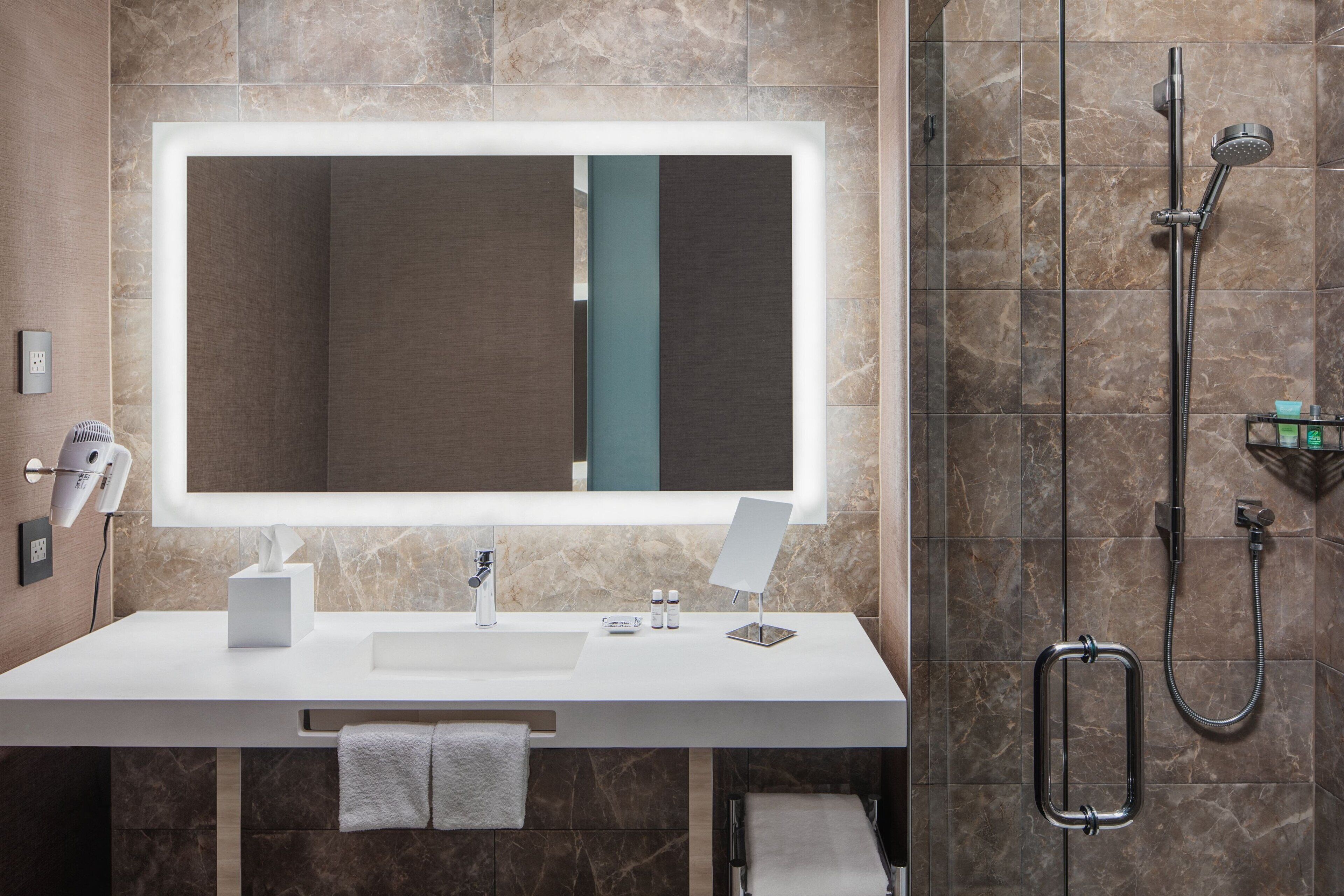 Une salle de bain moderne avec un grand miroir, un lavabo blanc, une douchette à main et un porte-serviettes.