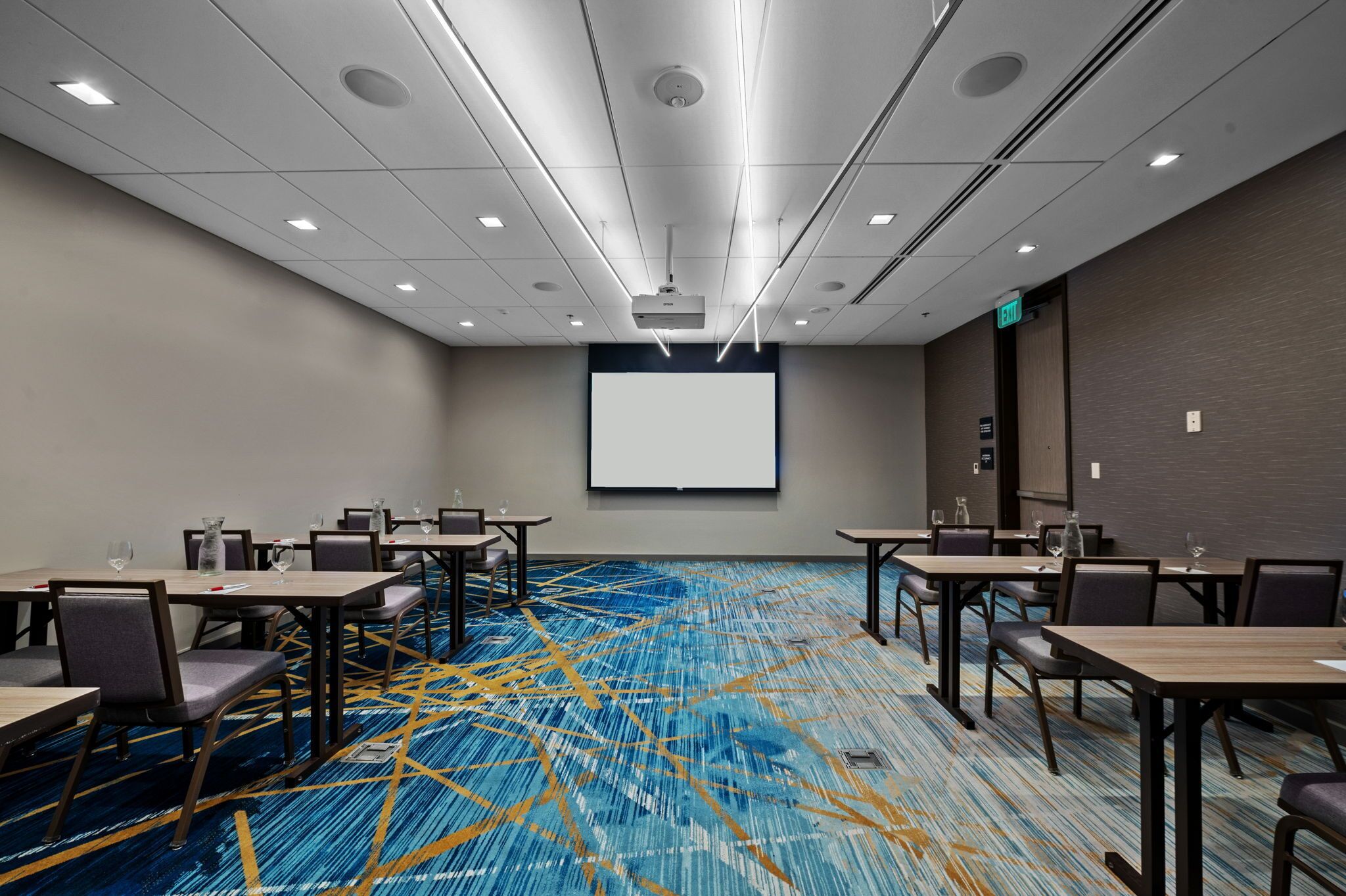 A conference room with a large screen, multiple tables, and chairs.