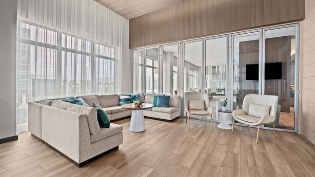 A spacious living room with a large sectional sofa, a coffee table, and a glass door leading to another room. - AC Hotel by Marriott Fort Lauderdale Airport (Dania Beach)