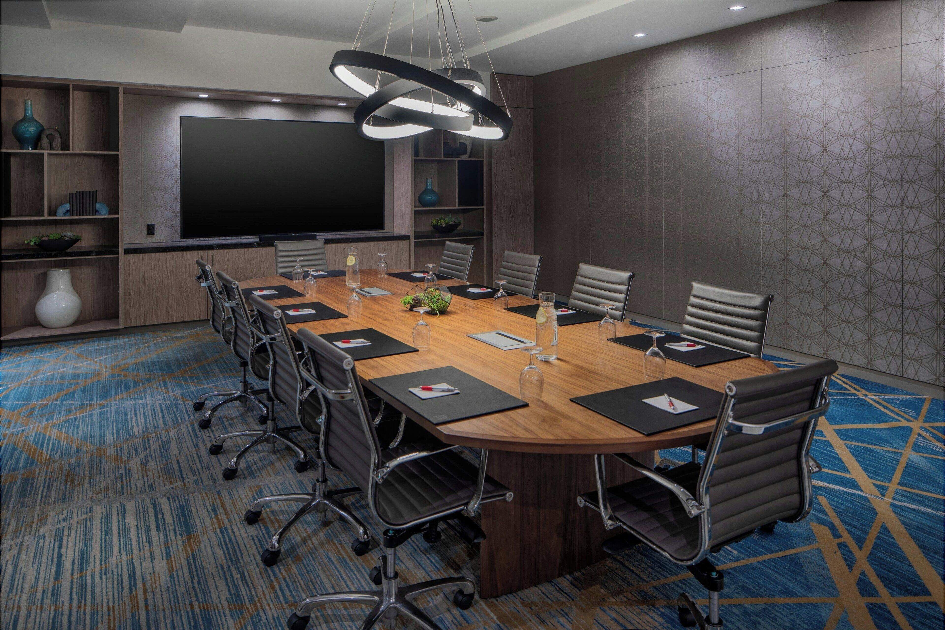 Una sala de conferencias con una mesa grande, sillas, un televisor de pantalla plana y una lámpara decorativa.