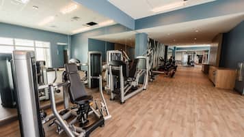 Un gimnasio con diversas máquinas de ejercicio, un espejo grande y suelo de madera.