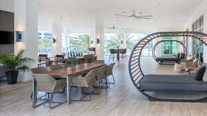A spacious, modern lounge area with a wooden dining table, wicker chairs, and a comfortable seating area with a sofa and armchairs. - AC Hotel by Marriott Fort Lauderdale Airport (Dania Beach)