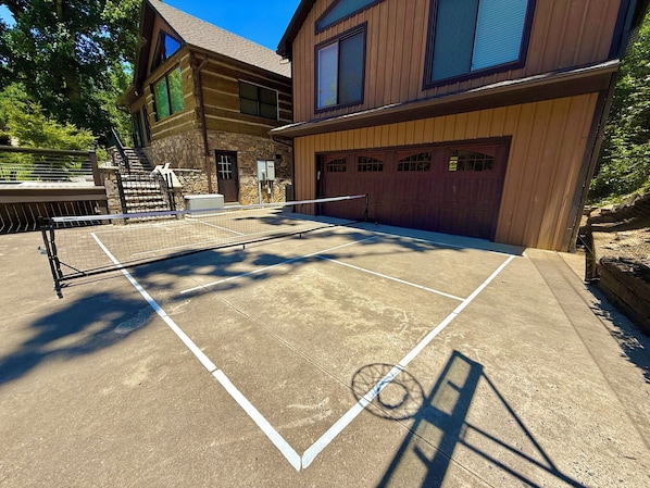 Una cancha de tenis con red, rodeada por un edificio de piedra y un garaje de madera.