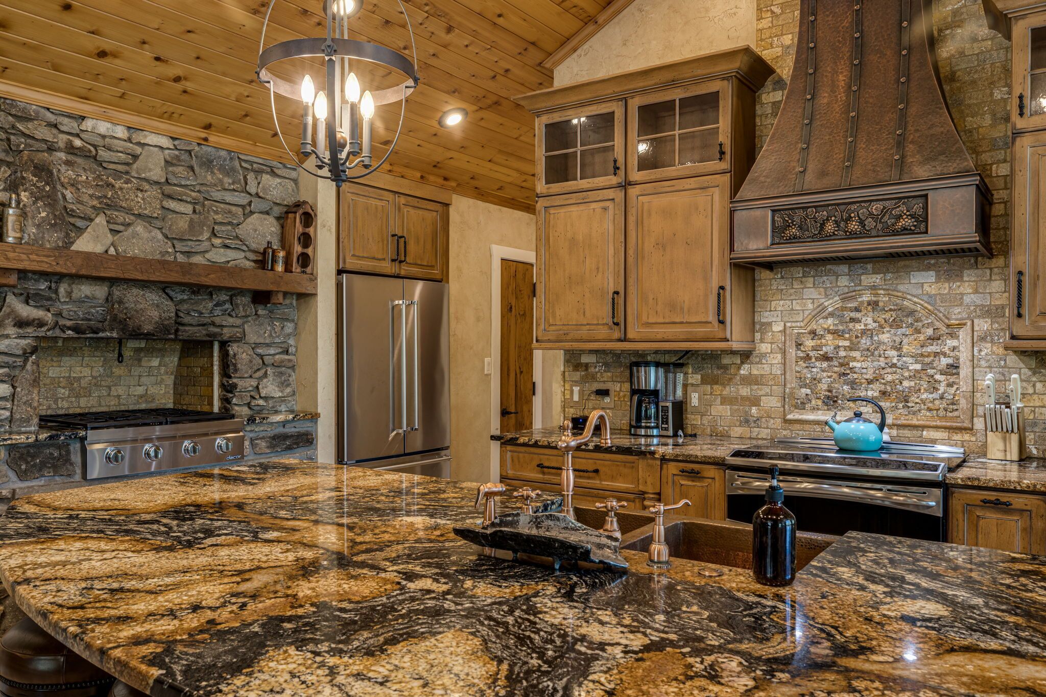 A kitchen with granite countertops, stainless steel appliances, wooden cabinets, and a stone fireplace.