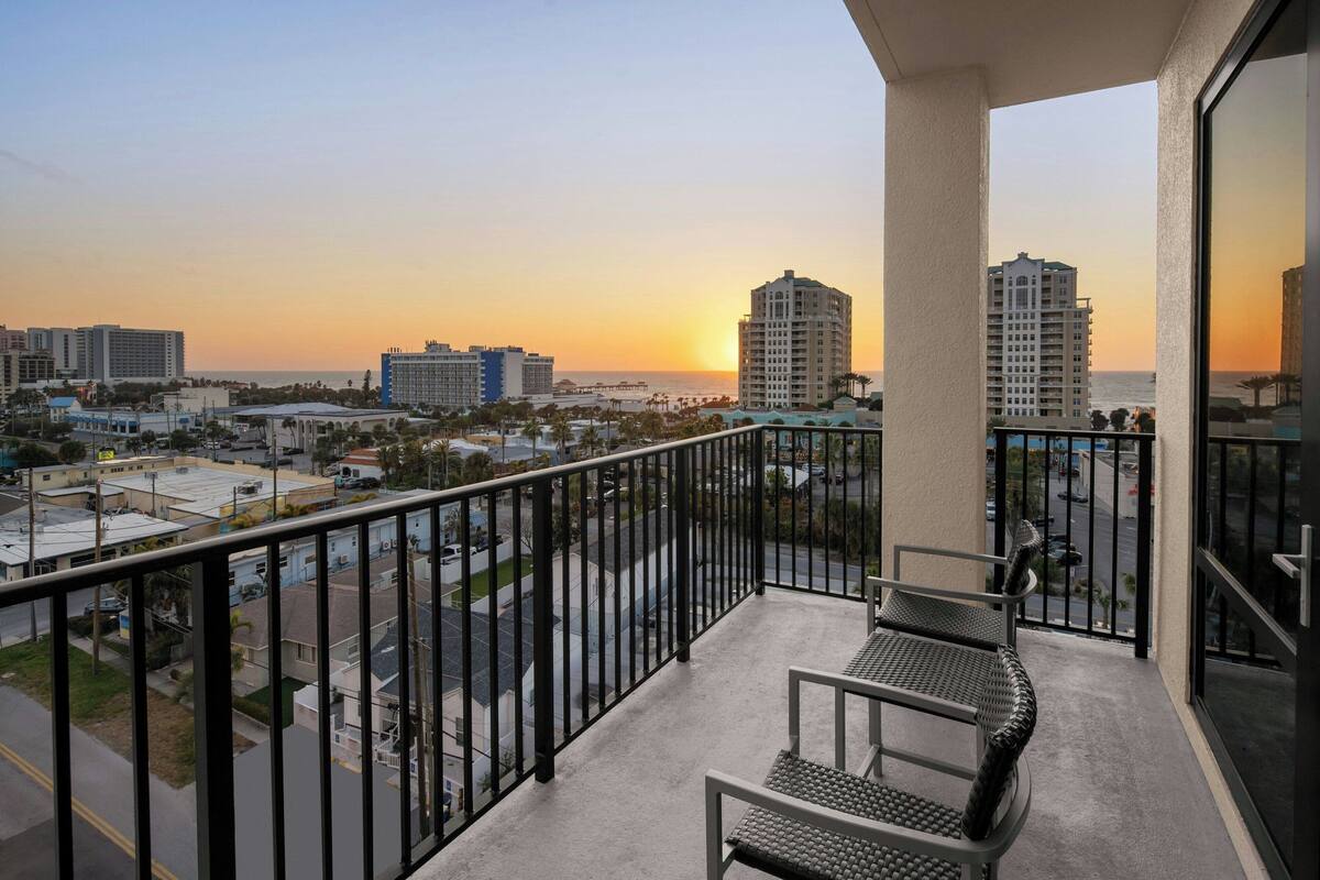 A balcony with a view of a cityscape and the ocean at sunset.
