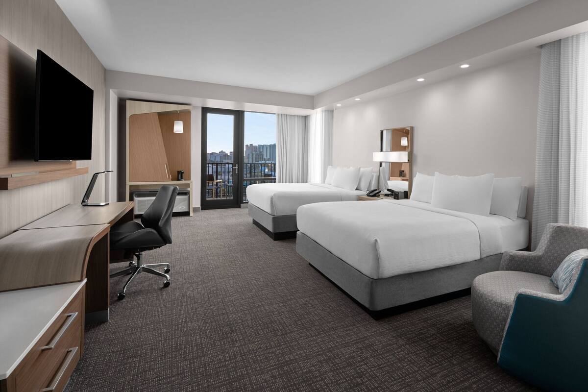A hotel room with a large bed, a desk, a chair, and a TV.
