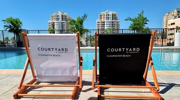 Dos sillas de playa con la etiqueta 'Courtyard by Marriott' en Playa Clearwater, con una piscina y edificios al fondo.