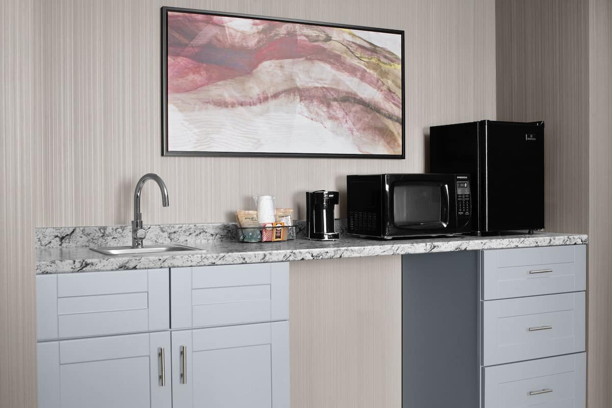 A kitchen with a marble countertop, a black microwave, a coffee maker, and a framed abstract painting on the wall.
