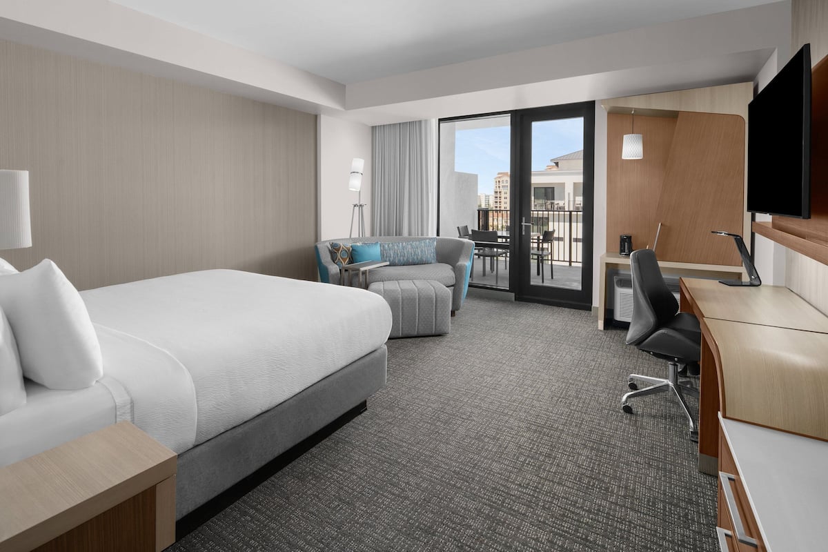 A modern hotel room with a large bed, a sofa, a desk, and a TV.