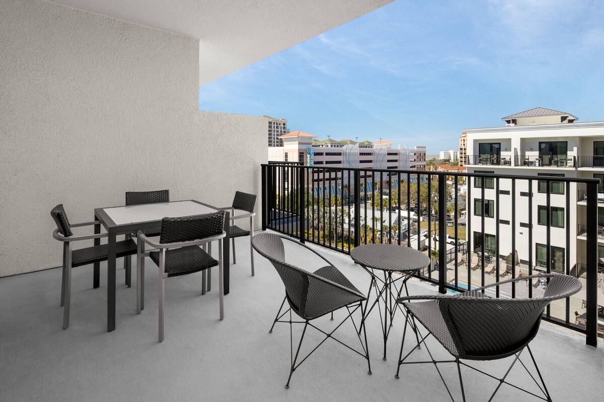 A balcony with a table and chairs, a view of buildings, and a clear sky.