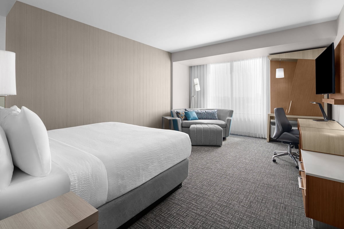 A hotel room with a large bed, a sofa, a desk, and a TV.